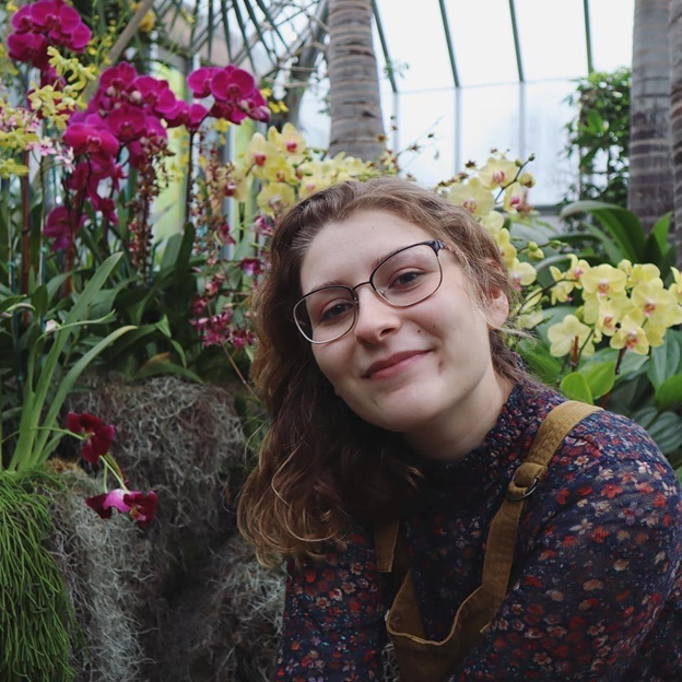 Kasie Chappell in front of orchids in a greenhouse